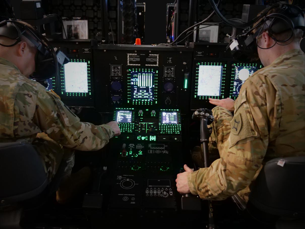 Two military personnel operating advanced aircraft control systems in a high-fidelity reconfigurable collective trainer cockpit simulator.